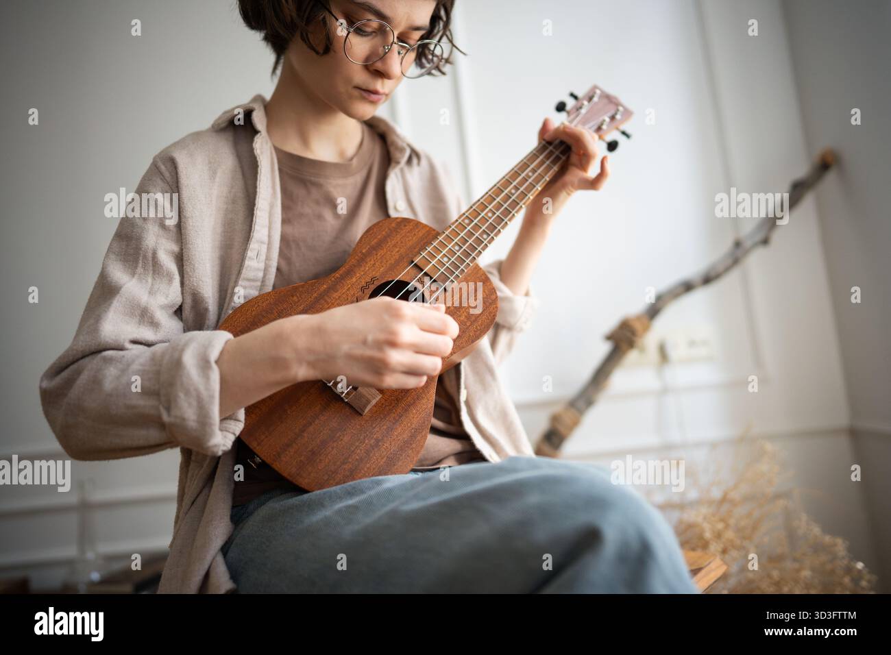 Junge Frau lernt neues Hobby, spielt auf hölzernen Ukulelen, zupft Saiten, genießt kreative Prozesse. Stockfoto