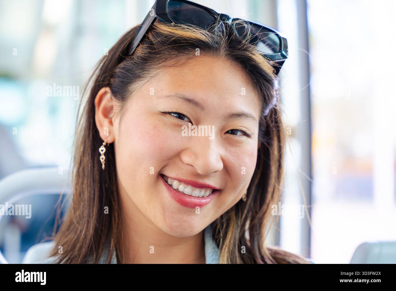 Lächelnde Frau, die in die Kamera blickt und drinnen mit natürlichem Tageslicht sitzt. Stockfoto