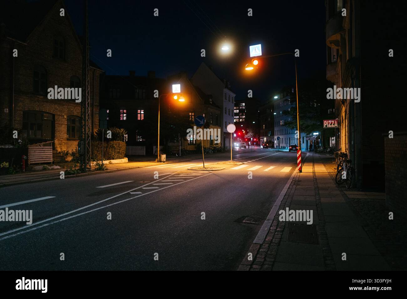 Eine friedliche nächtliche Szene einer leeren Straße in Kopenhagen, Dänemark, mit warmen Straßenlaternen und beleuchteten Fenstern, die die ruhige Stadt einfangen Stockfoto