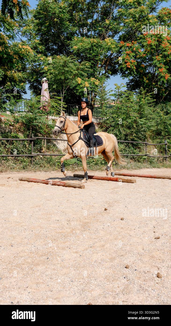 Ein Mädchen führt ihr Pferd geschickt über Hindernisse in einem Reitplatz im Freien. Sie demonstriert Konzentration und Kontrolle und hebt das Reittraining und hervor Stockfoto