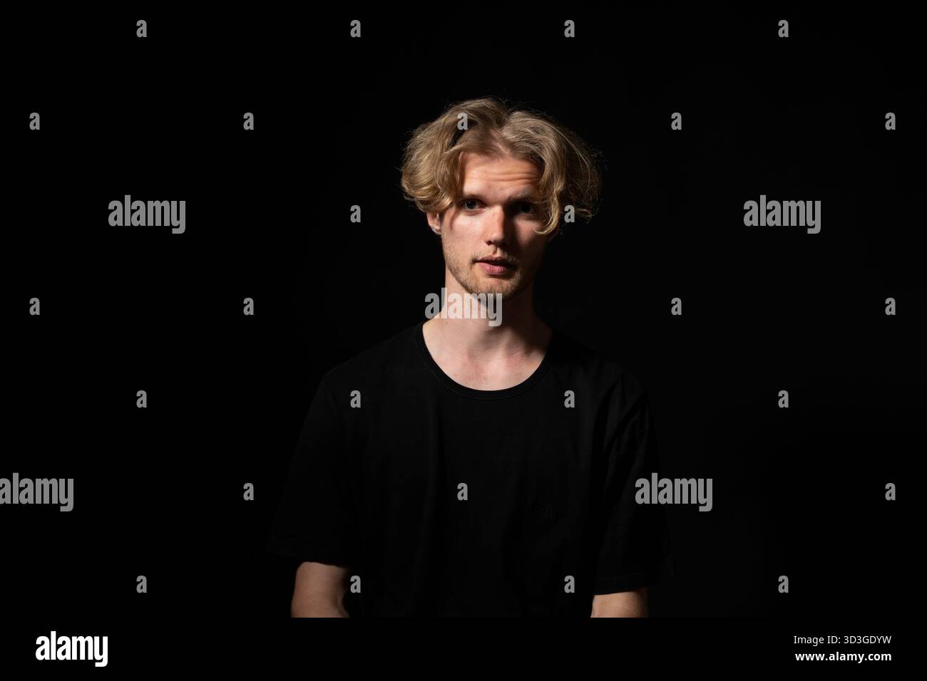 Ruhiger Mann in schwarzem Hemd, der unter stimmungsvoller Beleuchtung in dezentem Porträt nach vorne starrt Stockfoto