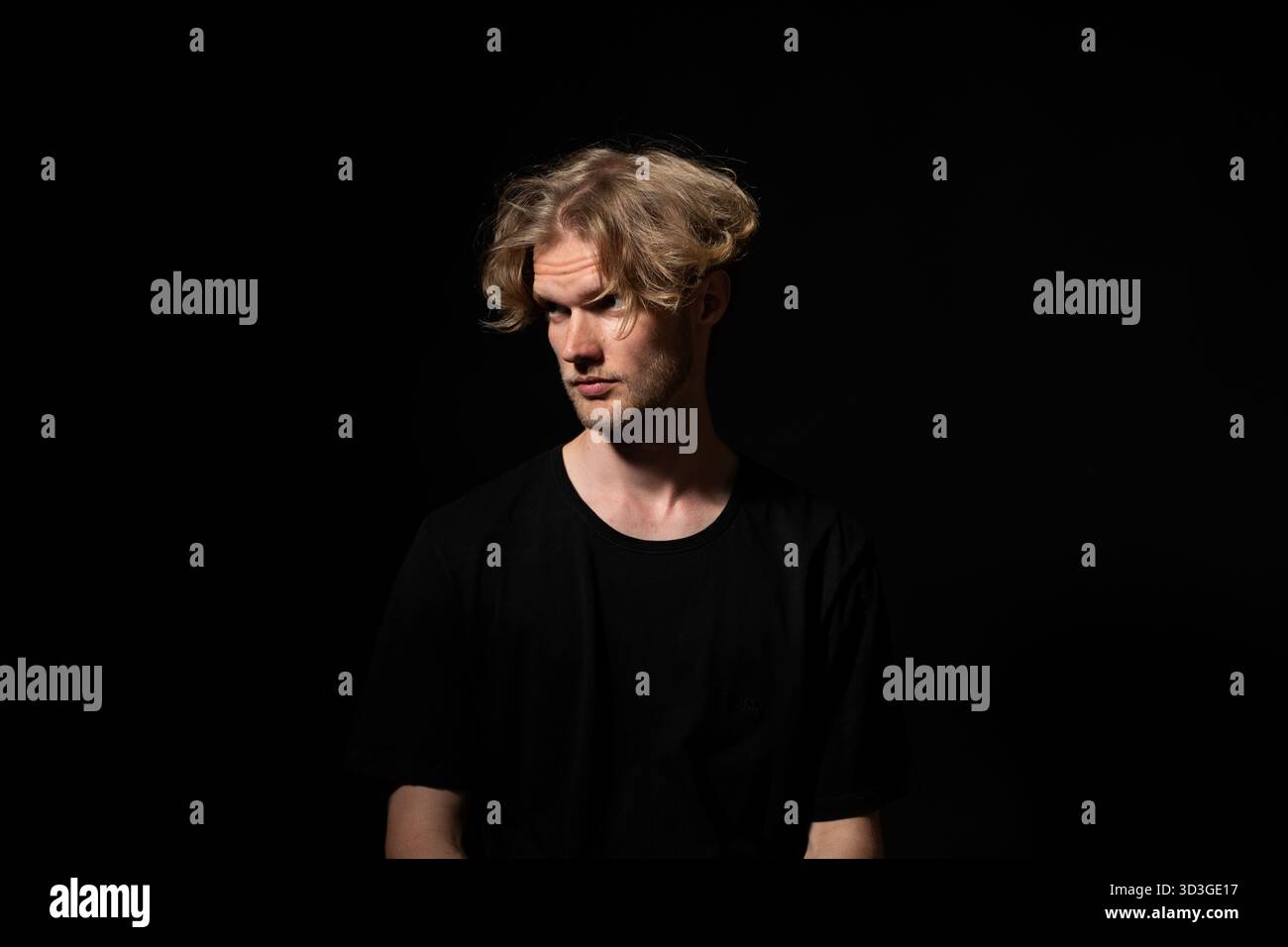 Verdächtiger Mann in schwarzem Hemd, der seitlich in dezentem Porträt mit dramatischer Beleuchtung schaut Stockfoto