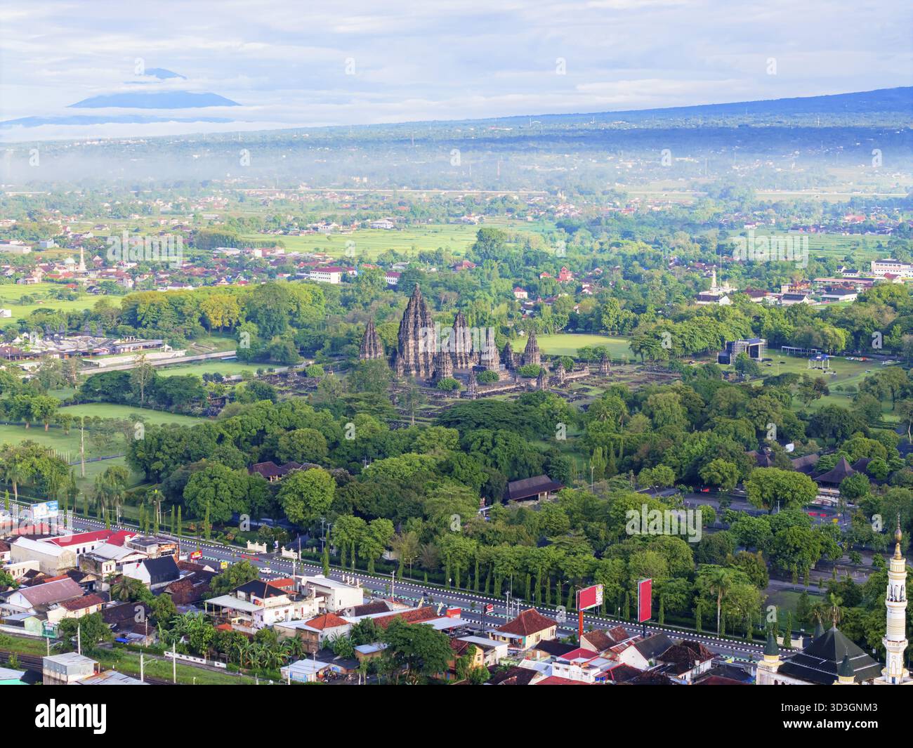 Blick aus der Vogelperspektive auf die antiken Tempel, die sich inmitten eines Meeres aus üppigen grünen Bäumen erheben, mit fernen Bergen, die den Horizont bemalen, Yogyakarta, Daerah Istimewa Yogya Stockfoto