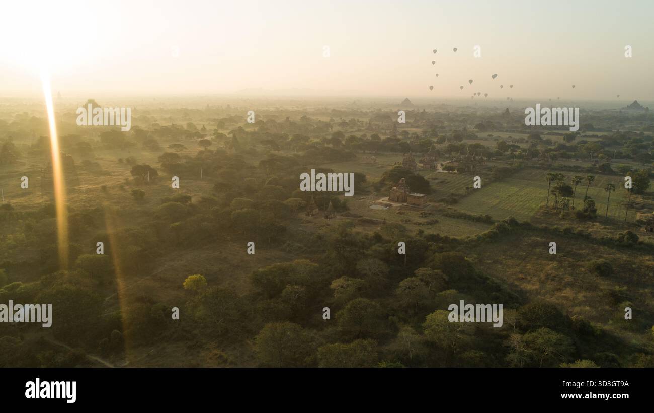 Aus der Vogelperspektive schweben Heißluftballons ruhig über antike Tempel und üppige Landschaften, die in das sanfte, goldene Licht der Morgenröte getaucht sind, Old Bagan, Mandalay Stockfoto