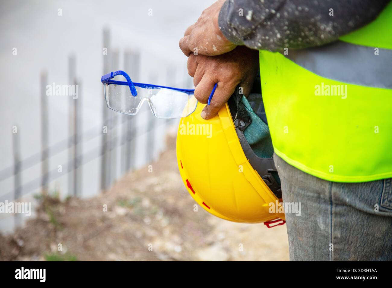 Arbeiter mit gelbem Helm und Schutzbrille auf der Baustelle im Freien, mit Schutzweste. Stockfoto