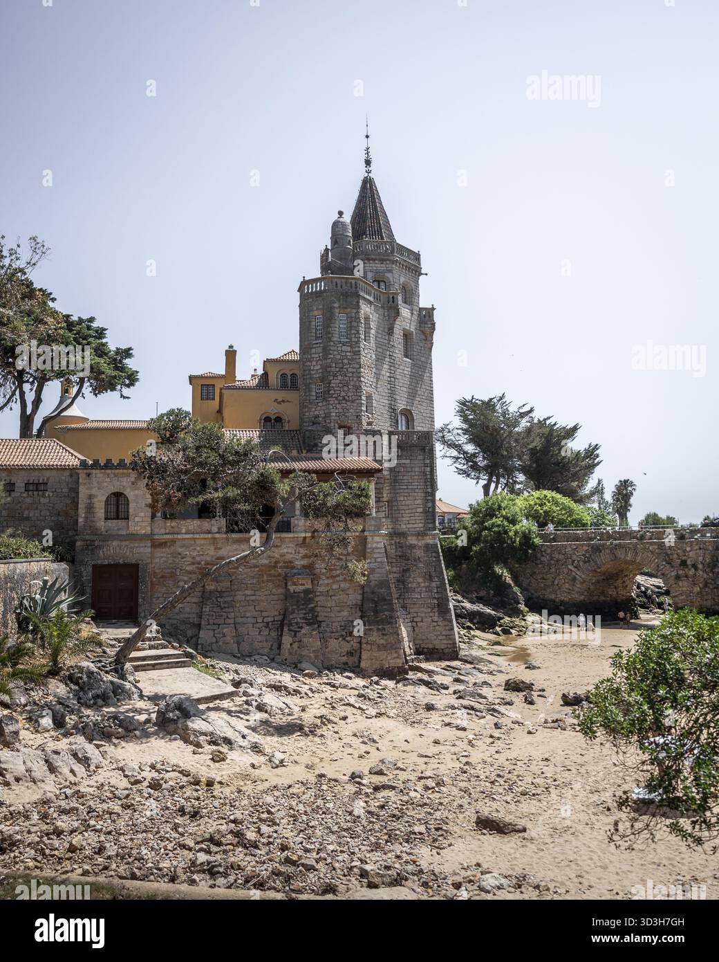 Der Blick auf die krasse Steinfestung mit ihrem hoch aufragenden Turm erhebt sich gegen den hellen Himmel, eine alte Steinbrücke über dem Sandstrand, Cascais, Lisbo Stockfoto