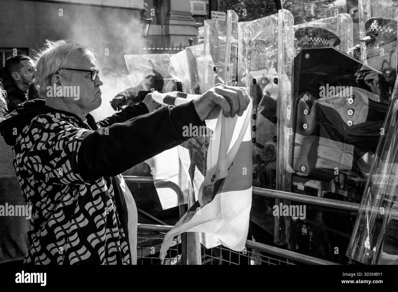 Ein Mann schwingt Ein Kreuz der St. George Flagge bei Metropolitan Police Officers, die hinter Riot Shields stehen, während der Unite the Kingdom Rally in London, Großbritannien. Stockfoto