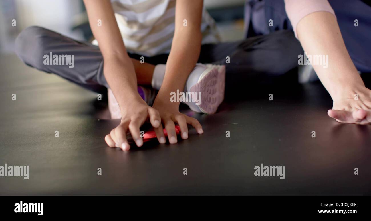 Das Kind wird mit gestreiften, dunklen Leggings auf der Studiomatte erreicht, der Erwachsene greift in Richtung eines kleinen roten Spielzeugs Stockfoto