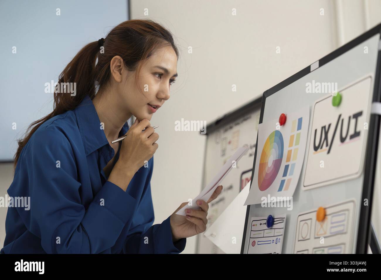 Ein fokussierter Designer analysiert kritische UX-UI-Designelemente, die auf einer Platine präsentiert werden, und zeigt einen innovativen Ansatz für die Entwicklung von Benutzeroberflächen Stockfoto