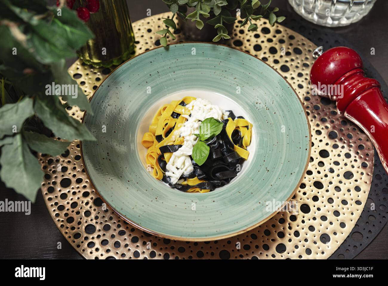 Essen, eleganter Teller mit schwarzer Tintenfischtinte und gelben Ei-Tagliatelle-Pasta mit cremiger Sauce und frischer Basilikumgarnitur, serviert in gehobenem Stil Stockfoto