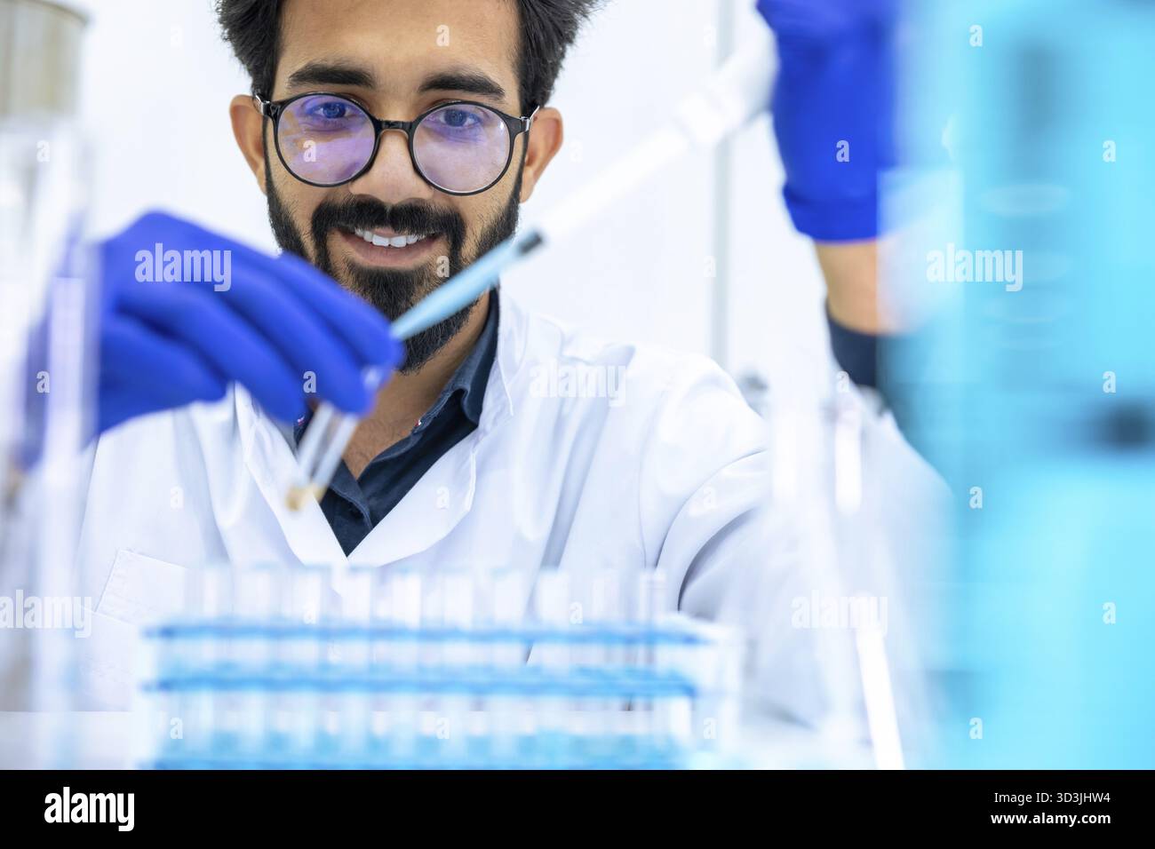 Mann Wissenschaftler mit Schutzhandschuhen Tropfen Chemikalien in Reagenzgläser, Biochemiker führt Experimente durch, um neue Medikamente zu entdecken, arbeitet in der Wissenschaft Stockfoto