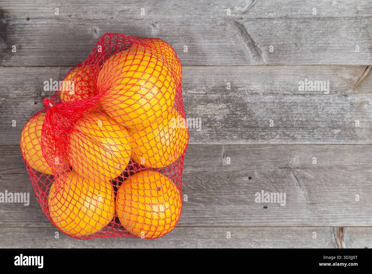 Hellgelbe Zitrusfrüchte in einem roten Netzbeutel auf rustikalen Holzbrettern. Stockfoto