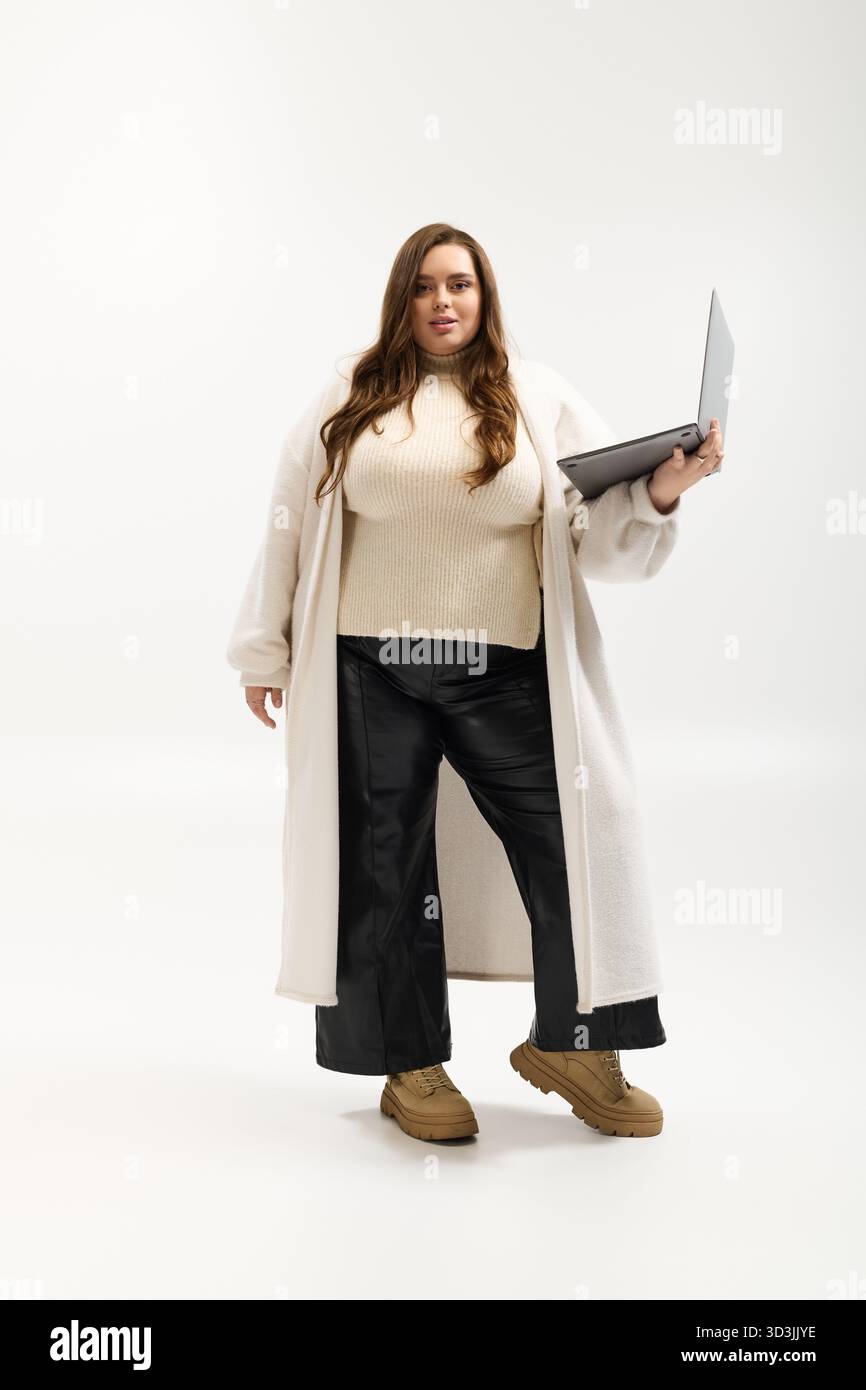 Eine junge Frau in Übergröße posiert selbstbewusst in einem gestrickten Winterpullover in einem hellen Studio. Stockfoto