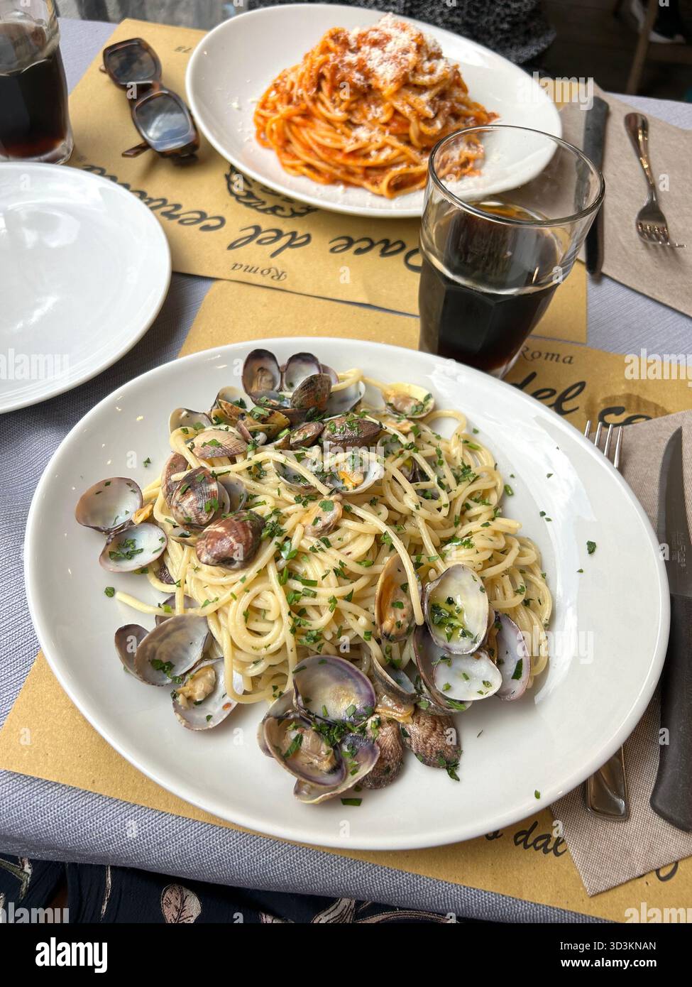 Tisch in einem Restaurant in Rom, Italien, mit zwei Tellern Pasta. Das nächste Gericht ist Spaghetti alle Vongole mit Muscheln, die in natürlichem Licht aufgenommen werden. Stockfoto