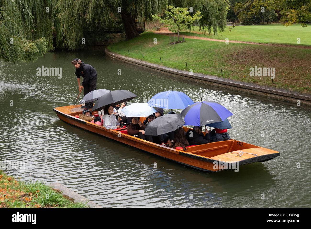 Touristen, die mit Regenschirmen bedeckt sind, während sie eine Punt River Tour im Regen auf dem Fluss Cam in the Back Cambridge England machen Stockfoto