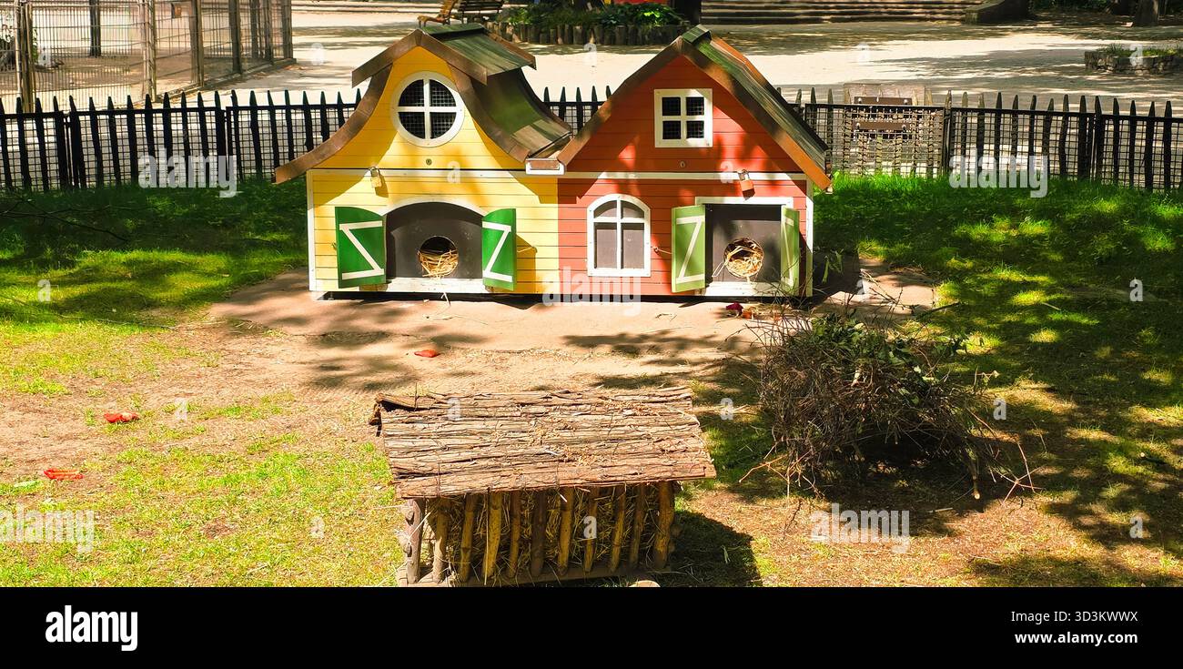 Farbenfrohe Tierhäuser befinden sich in einem sonnigen Park, umgeben von grünen Gras und Bäumen, die eine verspielte und einladende Atmosphäre schaffen. - Smartphone-aufgenommenes Stockfoto