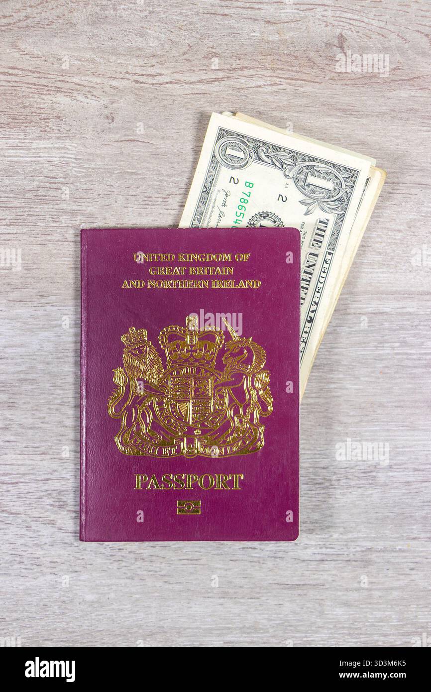 Britischer britischer Reisepass mit mehreren US-Dollar-Scheinen oder Banknoten auf einer hellen Holzoberfläche, die ein Reise- oder internationales Finanzkonzept darstellen Stockfoto