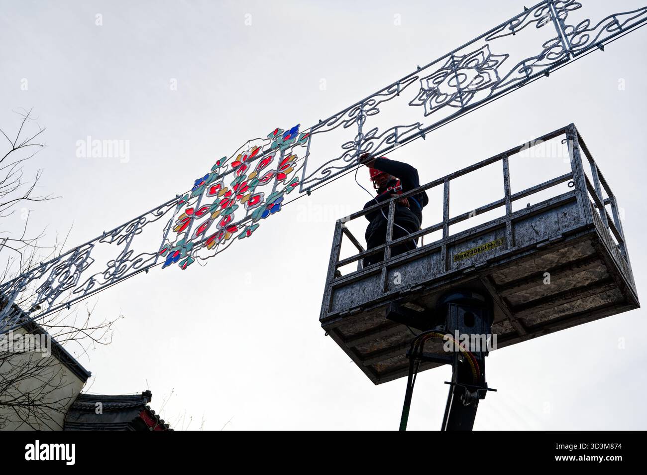 Arbeiter an einem Aufzug installieren in Peking vor dem chinesischen Neujahr einen farbenfrohen dekorativen Leuchtenrahmen Stockfoto