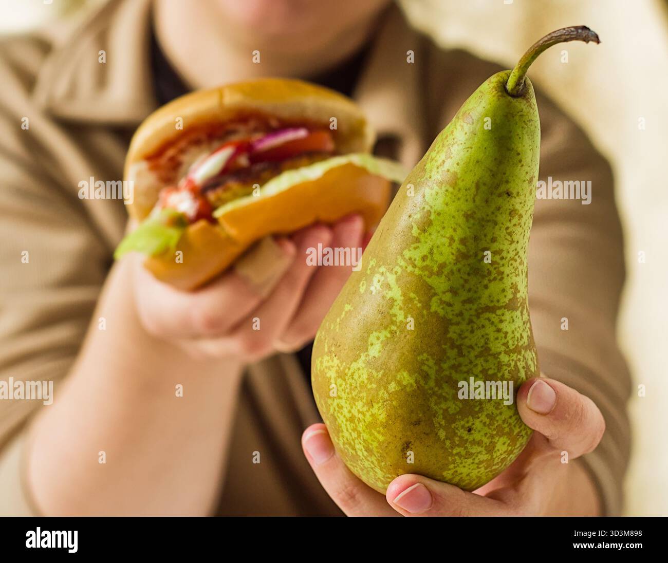 Die Hände der Frau halten sowohl eine frische grüne Birne als auch einen saftigen Hamburger, ein Konzept der Wahl der Nahrung gesund vs ungesund Stockfoto