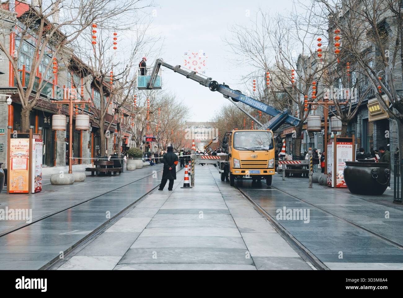 Im Winter installieren die Arbeiter mit einem Kranwagen entlang einer von Laternen gesäumten Allee festliche Straßendekorationen Stockfoto