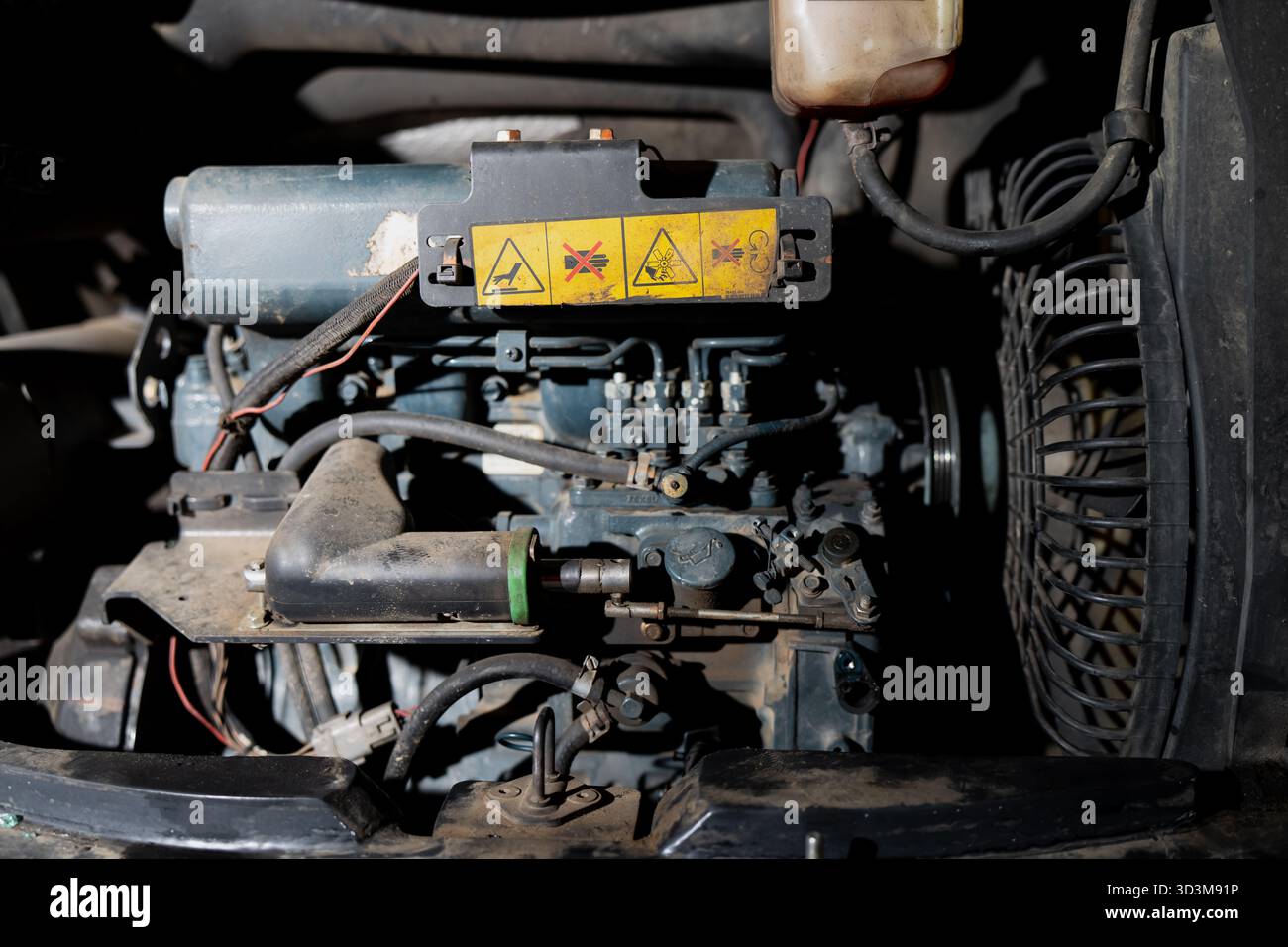 Nahaufnahme des Dieselmotorraums mit Warnsymbolen, Kraftstoffeinspritzanlage, Kühlerlüfter und mechanischen Anschlüssen, die Industriemaschinen zeigen Stockfoto