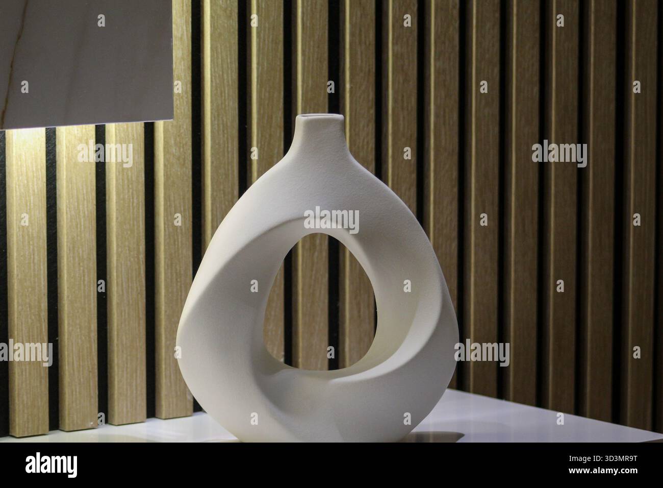 Künstlerische Keramikvase mit hohler Mitte und glatter matter Textur, stehend auf einer weißen Oberfläche mit warmer Beleuchtung. Stockfoto
