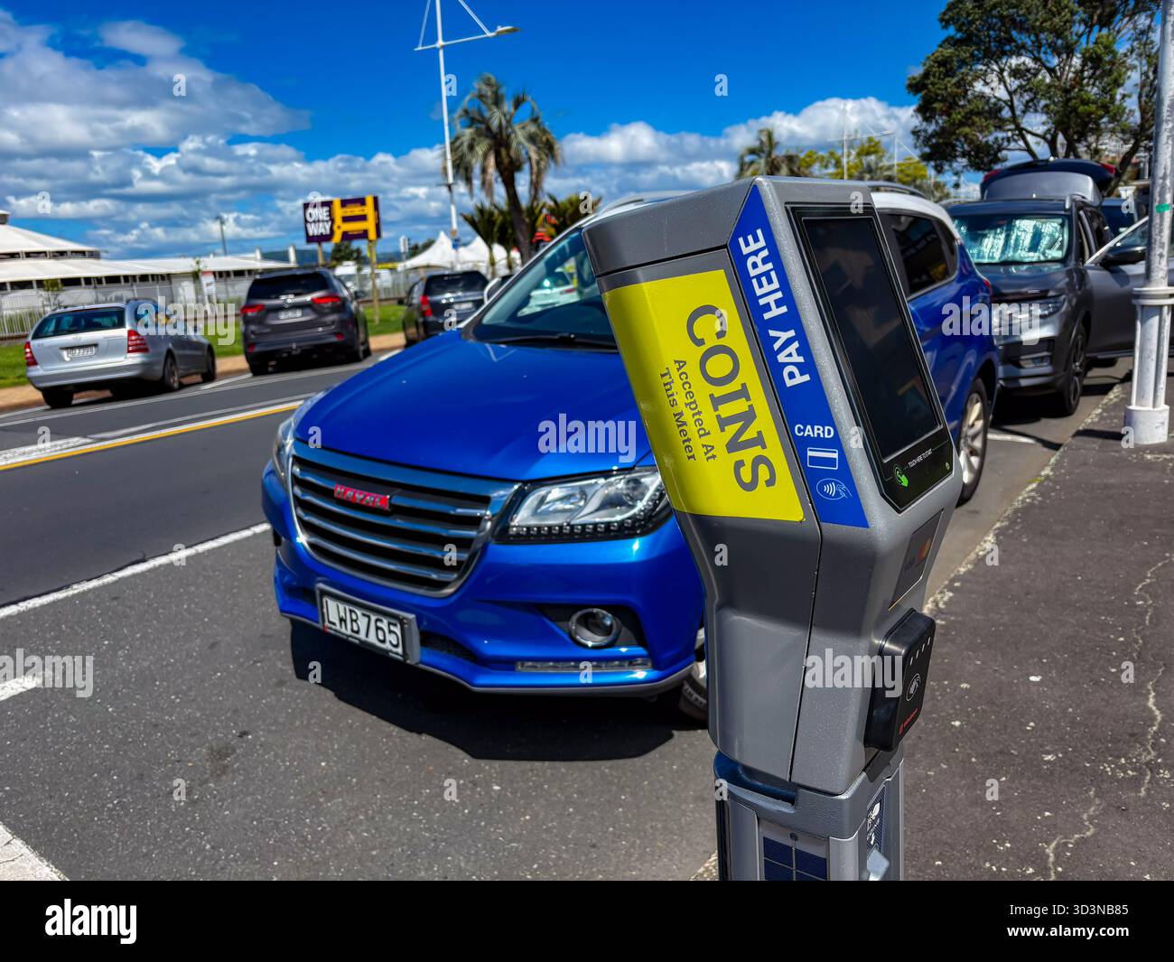 Eine moderne graue Parkuhr, die Münzen und Karten akzeptiert, steht im Vordergrund und die geparkten Autos sind auf einer Straße in Tauranga, New Zea, zu sehen Stockfoto