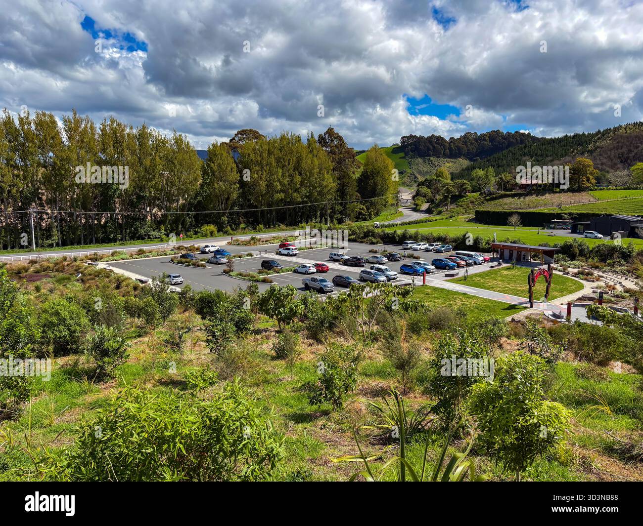 Papamoa Hills Regional Park. Blick von oben auf den Hauptparkplatz voller Autos, eingebettet in sanfte Hügel, dichte Bäume und eine Straße mit Tradition Stockfoto