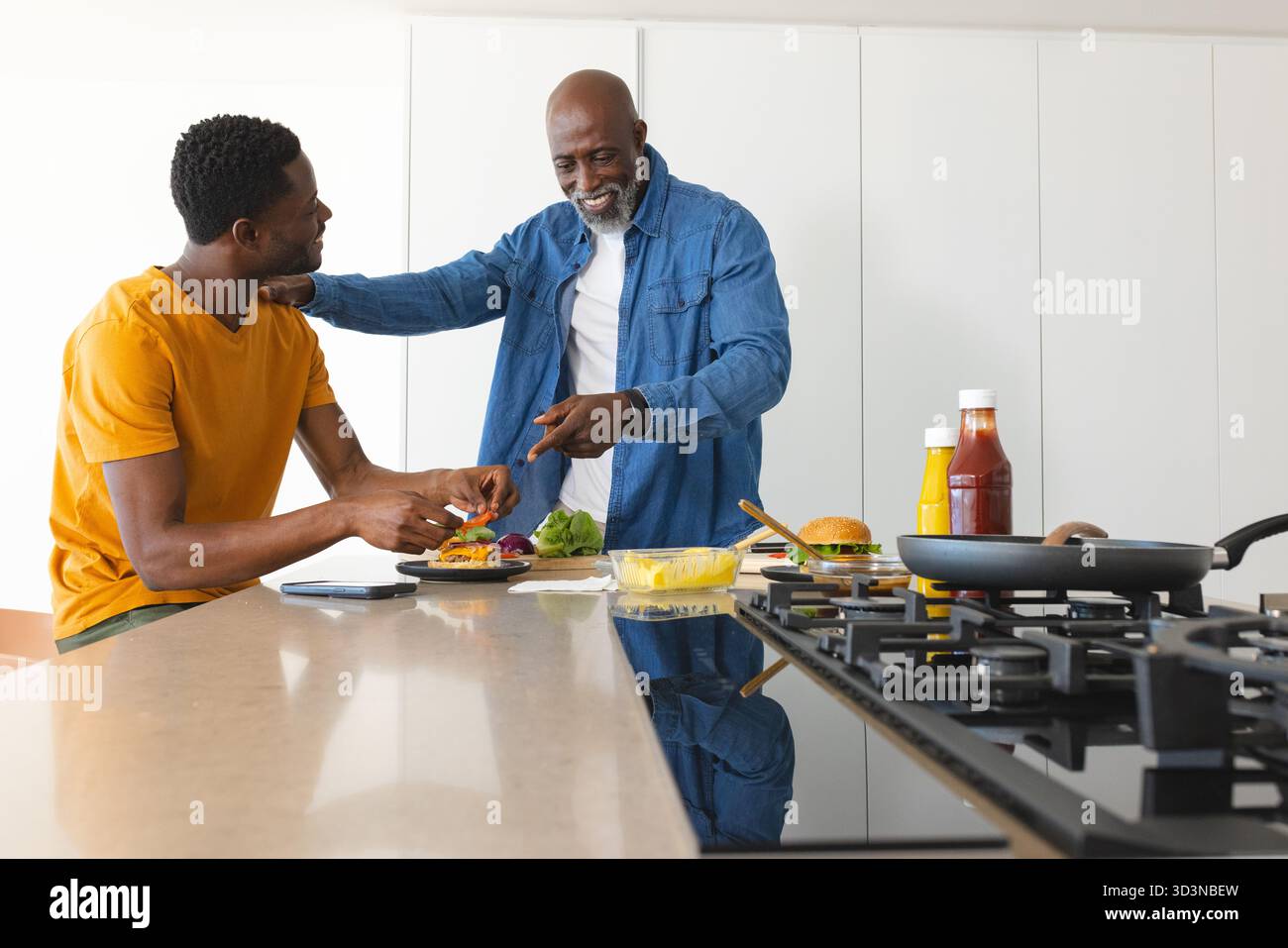 Afroamerikaner Vater und Sohn bauen, Burger in der Küche zubereiten, mit Smartphone und Pfanne Stockfoto