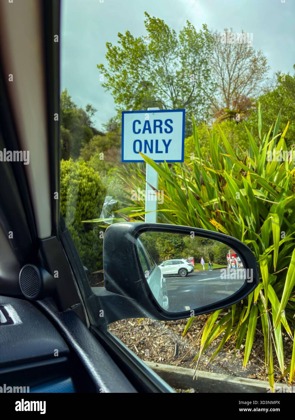 „Nur Fahrzeuge“-Schild, das einen eingeschränkten Parkbereich anzeigt, sichtbar vom Fahrzeuginnenraum, mit einem Seitenspiegel, der einen weißen SUV reflektiert. Stockfoto