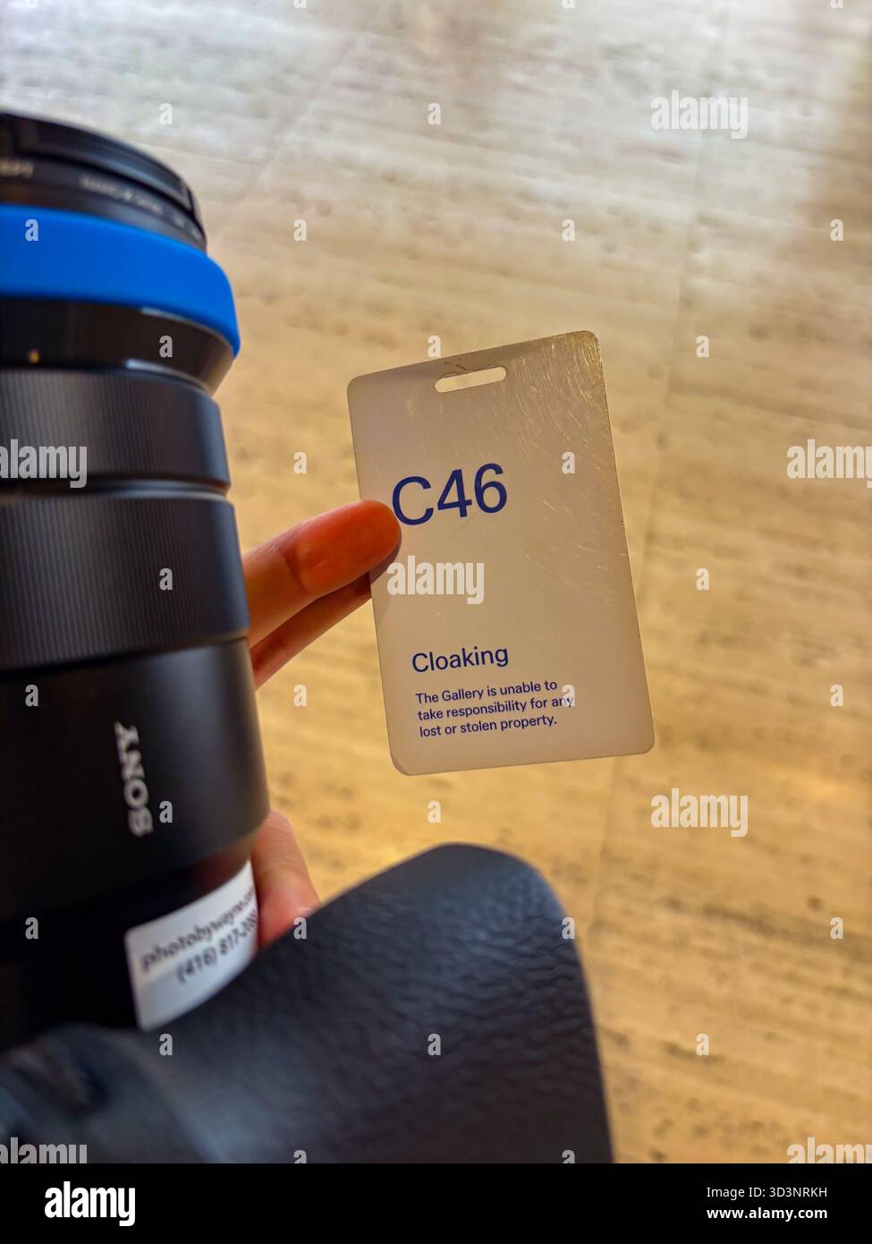 Garderobenpass C46, der von einer Hand gehalten wird, mit einem Haftungsausschluss bezüglich der „The Gallery“-Nichtverantwortung für verlorene Sachen, mit einem Kameraobjektiv von Sony in t Stockfoto
