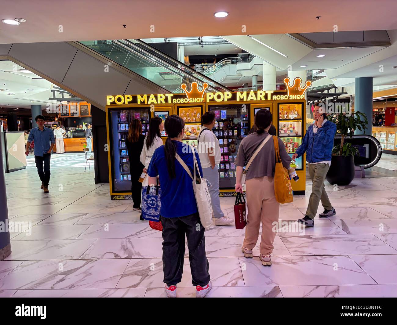 Pop Mart RoboShop Verkaufsautomaten, die Spielzeug aus der Blindbox verkaufen, werden in einem modernen Einkaufszentrum gesehen, in dem Kunden stöbern. Rolltreppen befinden sich in der Th Stockfoto