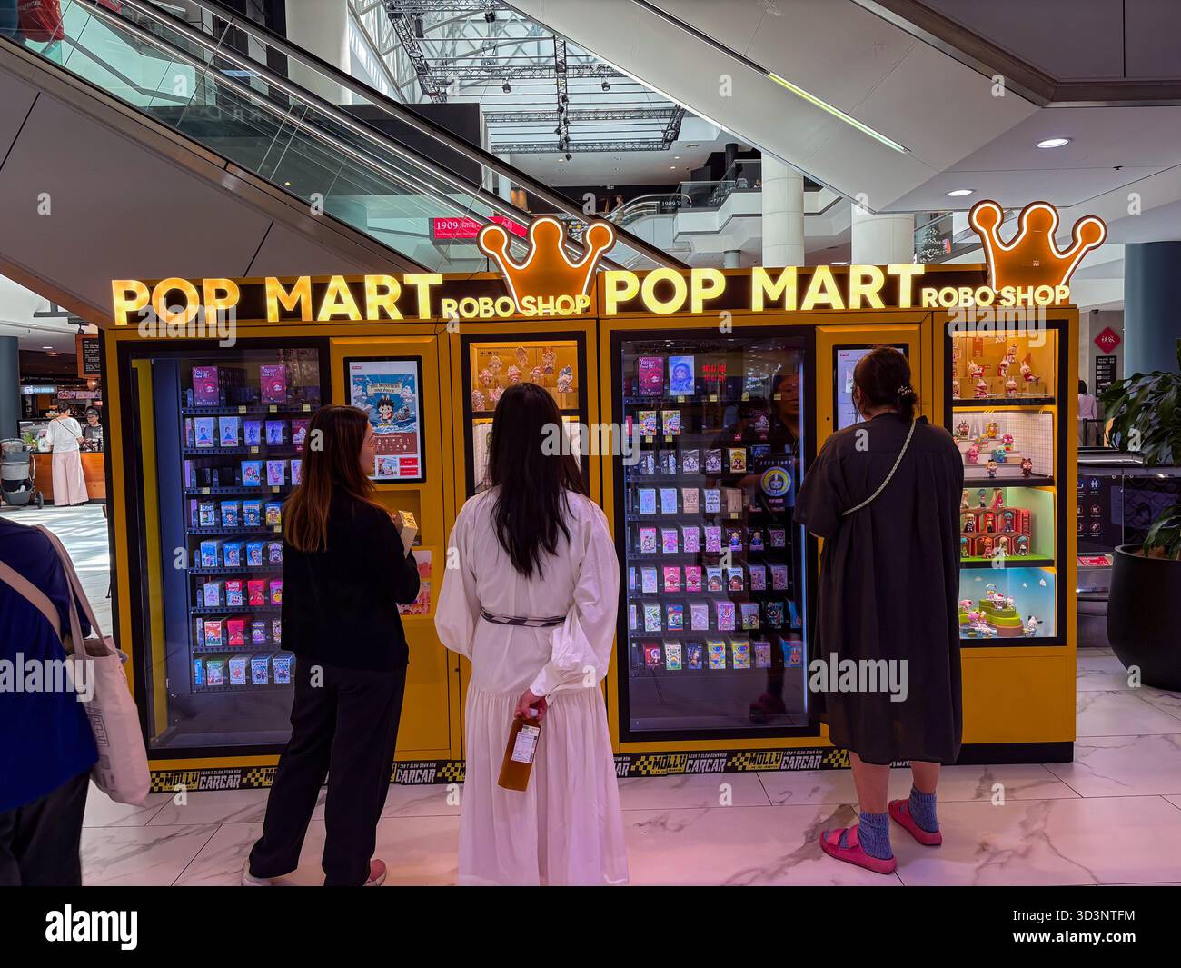 Pop Mart Robo Shop Verkaufsautomaten mit Sammlerspielzeug für Blindkästen, die von drei Frauen in einem modernen Einkaufszentrum angesehen werden. Stockfoto