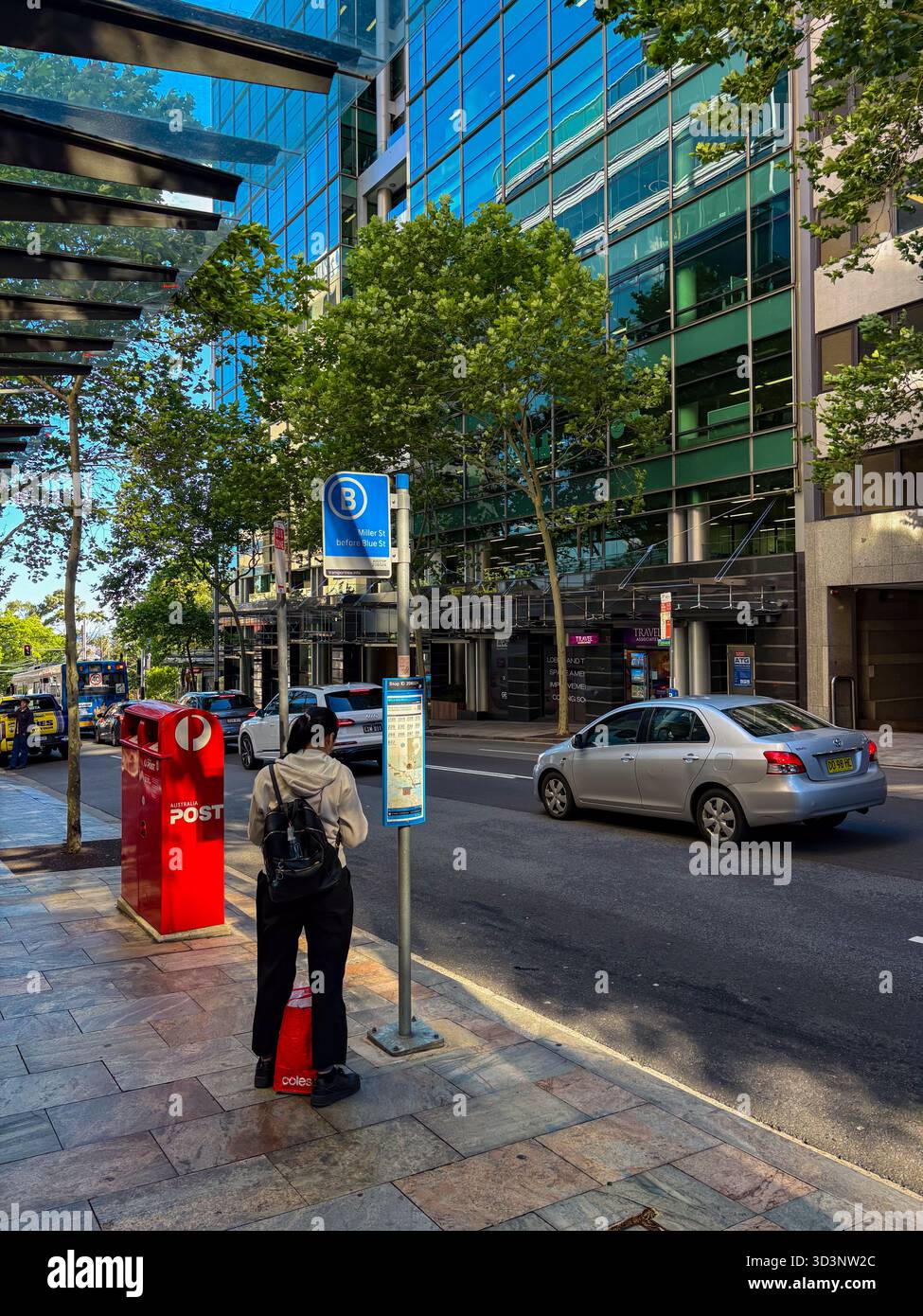 Eine Straßenszene in North Sydney, Australien, zeigt eine Person, die an einer Bushaltestelle neben einem roten Postfach der Australia Post wartet, mit einem silbernen Auto, das an einem vorbeifährt Stockfoto
