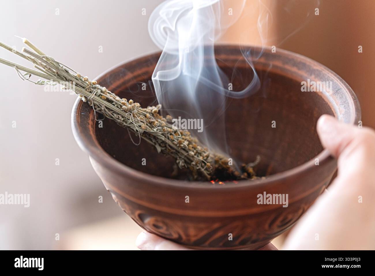 Beifuß-Rauchstab schwelt in einer Tonschale während eines Reinigungsrituals. Kräuterweihrauch wird zur Reinigung von Raum, Schutz, Meditation und Re verwendet Stockfoto