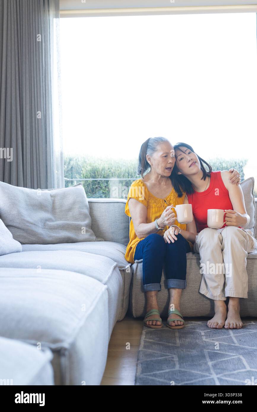 Asiatische Familie mit warmen Getränken im gemütlichen Wohnzimmer, mit weißen Tassen, Kopierraum Stockfoto