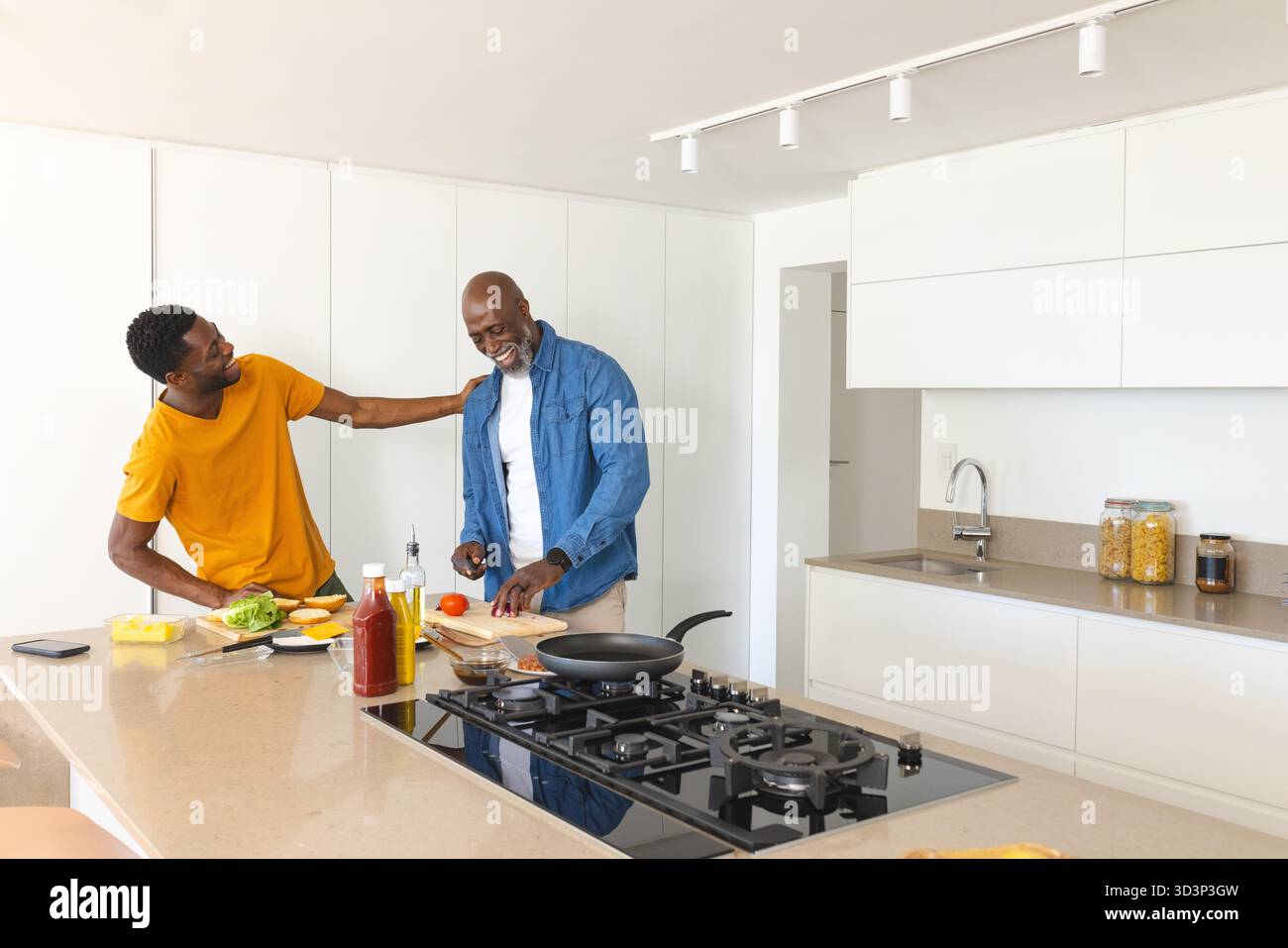 Afroamerikaner Vater und Sohn kochen, Tomaten auf Kücheninsel schneiden, mit Smartphone Stockfoto