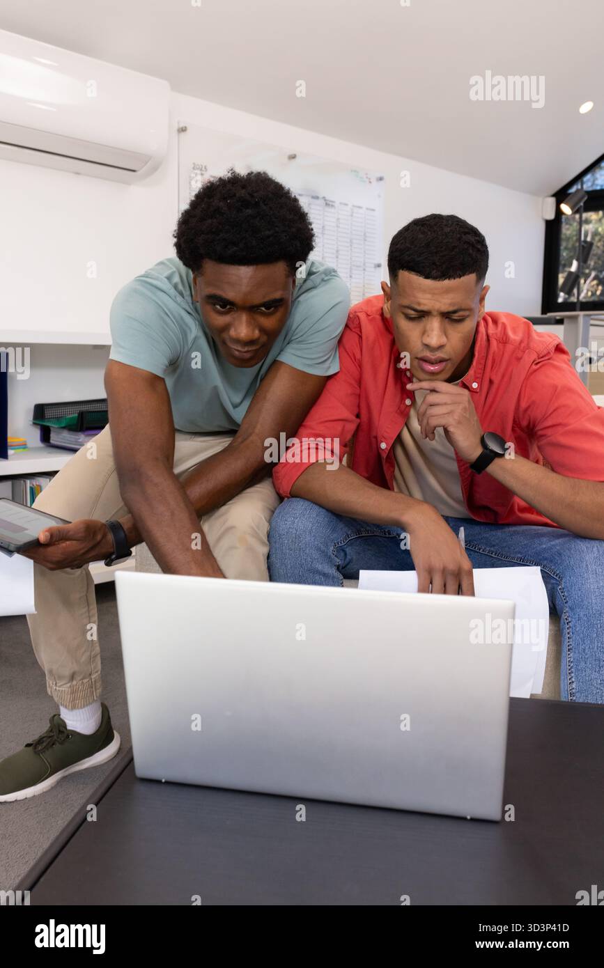 Verschiedene männliche Kollegen, die Dokumente über Laptops und Papiere im Untersuchungsraum überprüfen, fördern die Teamarbeit Stockfoto