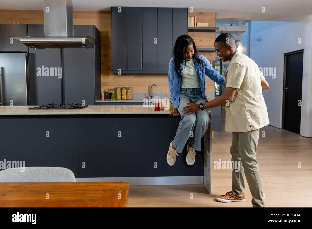 Afroamerikaner sitzen und plaudern auf der Kücheninsel mit Getränken zum Mitnehmen und Glasgläsern Stockfoto