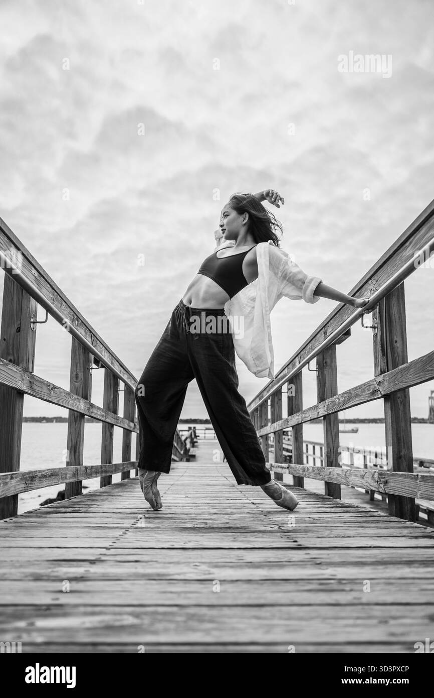 Tänzer, der zeitgenössische Ballettpositionen auf dem hölzernen Pier aufführt Stockfoto