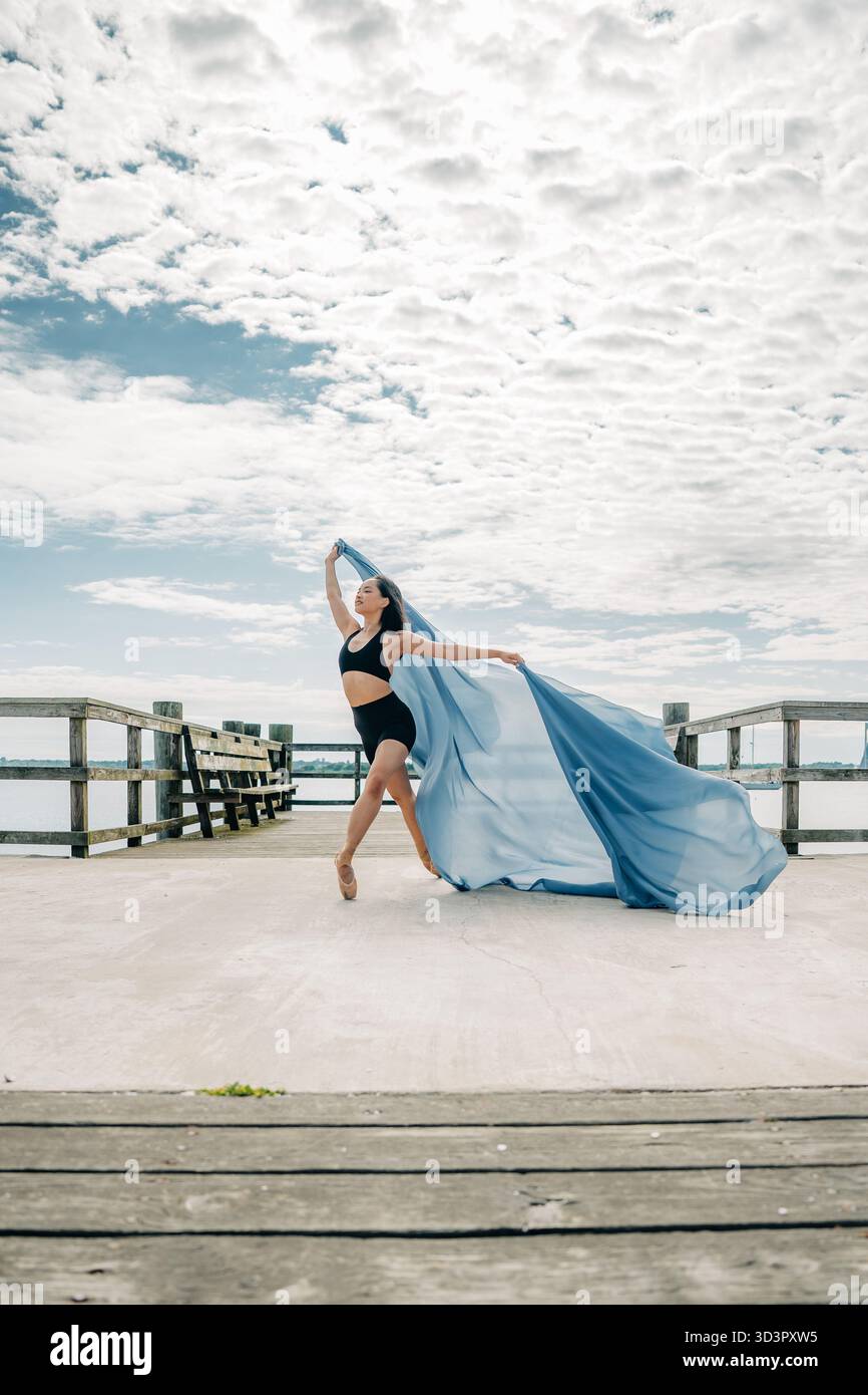 Ballerina tanzt anmutig mit blauem Stoff auf dem Pier Stockfoto