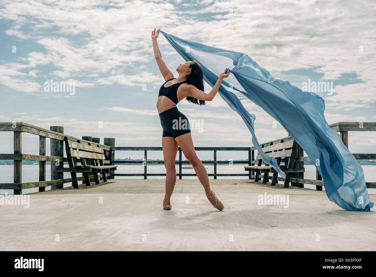 Balletttänzerin mit blauem Stoff am Pier Stockfoto