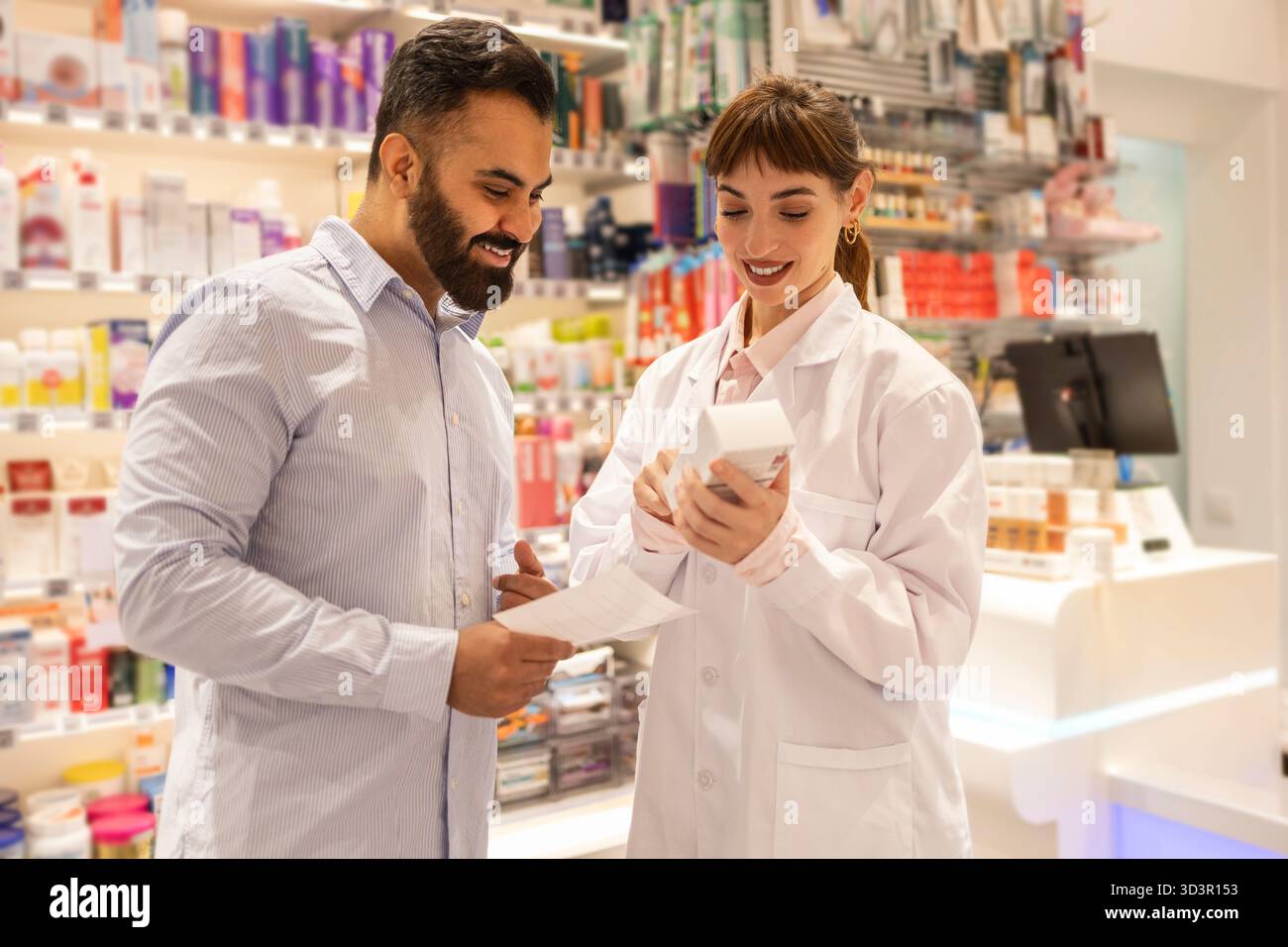 Ein Apotheker in einem weißen Laborkittel hilft einem Kunden mit einem Medikamentenpaket und bietet fachkundigen Rat. Im Hintergrund der Apotheke werden verschiedene Heilungen angezeigt Stockfoto