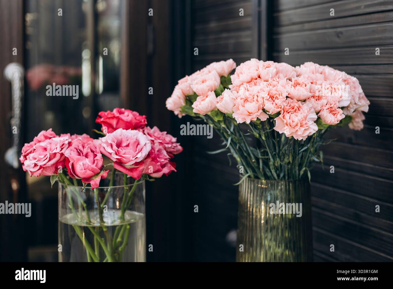 Elegante rosafarbene Nelken und Rosen in Glasvasen werden in einem gemütlichen Blumenladen ausgestellt und schaffen ein bezauberndes und ästhetisches Blumenarrangement, das noch mehr anregt Stockfoto