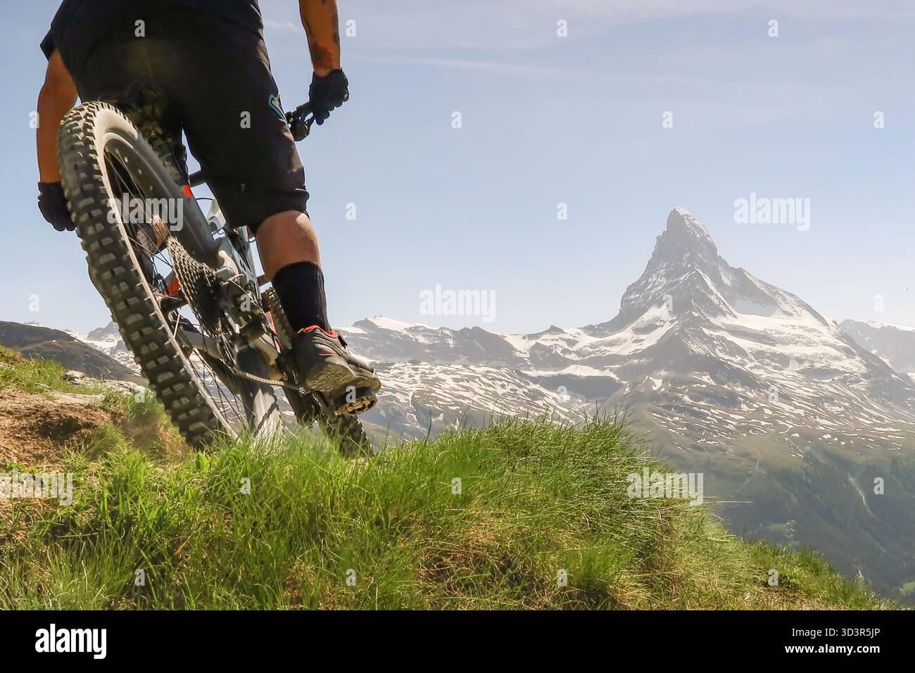 Ein Mountainbiker fährt auf einem üppigen Bergweg mit dem Matterhorn im Hintergrund und fängt den Nervenkitzel des Radfahrens in der atemberaubenden Landschaft ein Stockfoto