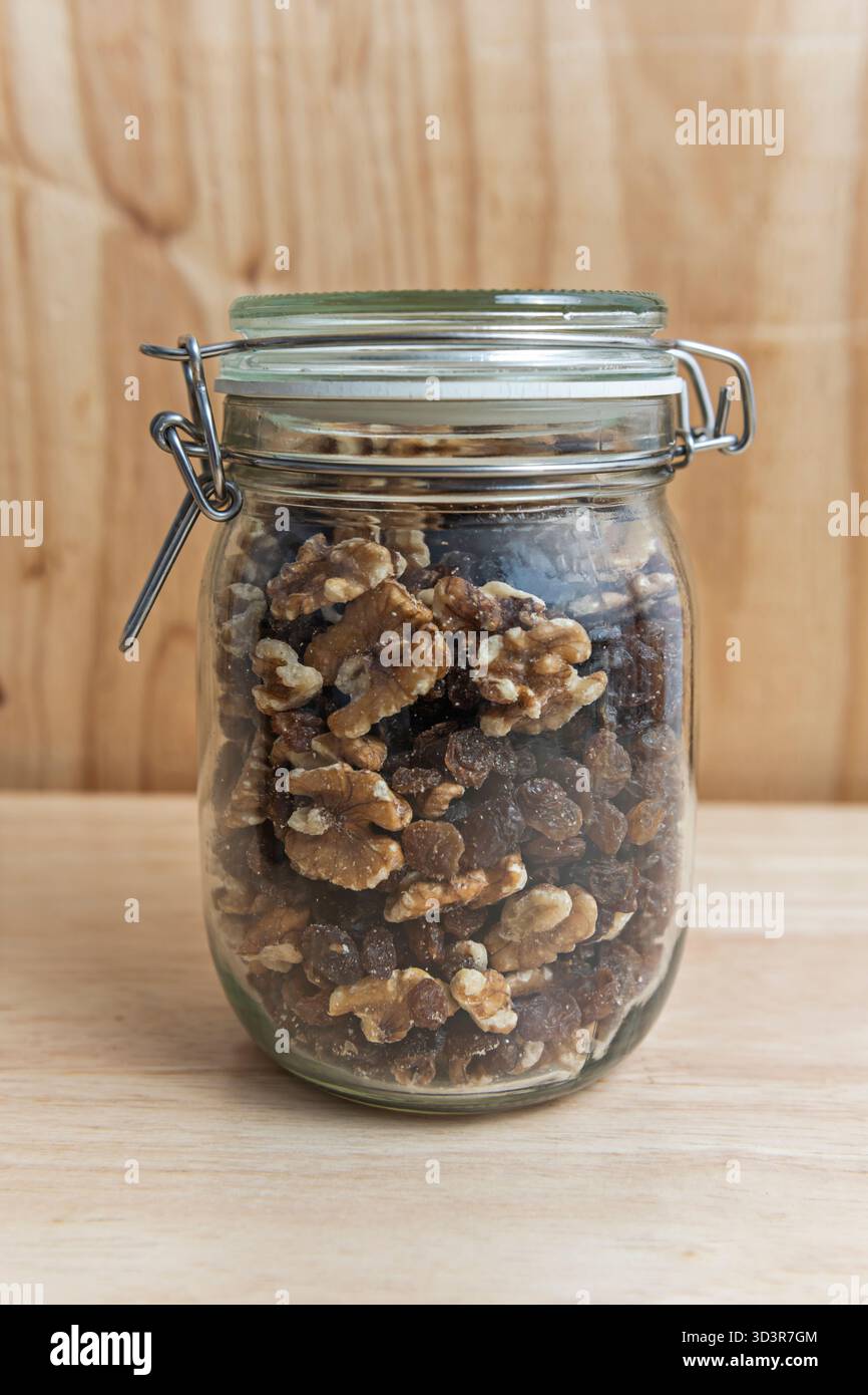 Die zerknitterte, erdige Textur der schalenförmigen Walnüsse sammelt sich am Boden des Glasbehälters an und bildet einen optischen Kontrast zur natürlichen Körnung des Stockfoto