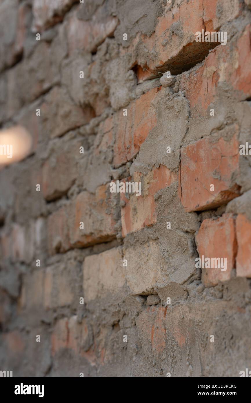 Nahaufnahme einer Ziegelmauer im Bau, mit unebenem Mörtel und freiliegenden orangen Ziegeln. Strukturierte Oberfläche vermittelt städtische, industrielle und renovierende Ästhetik. Vertikales Foto, selektiver Fokus. Stockfoto