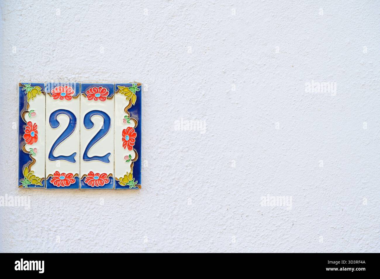 22 Hausnummer auf dekorativen Keramikfliesen und weißer Wand. Stockfoto