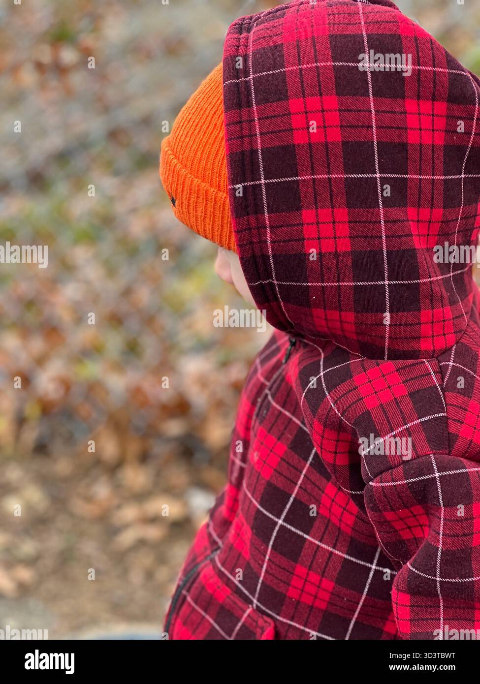 Kind in roter karierter Jacke und orangefarbener Strickmütze im Herbst - Smartphone-aufgenommenes Stockfoto