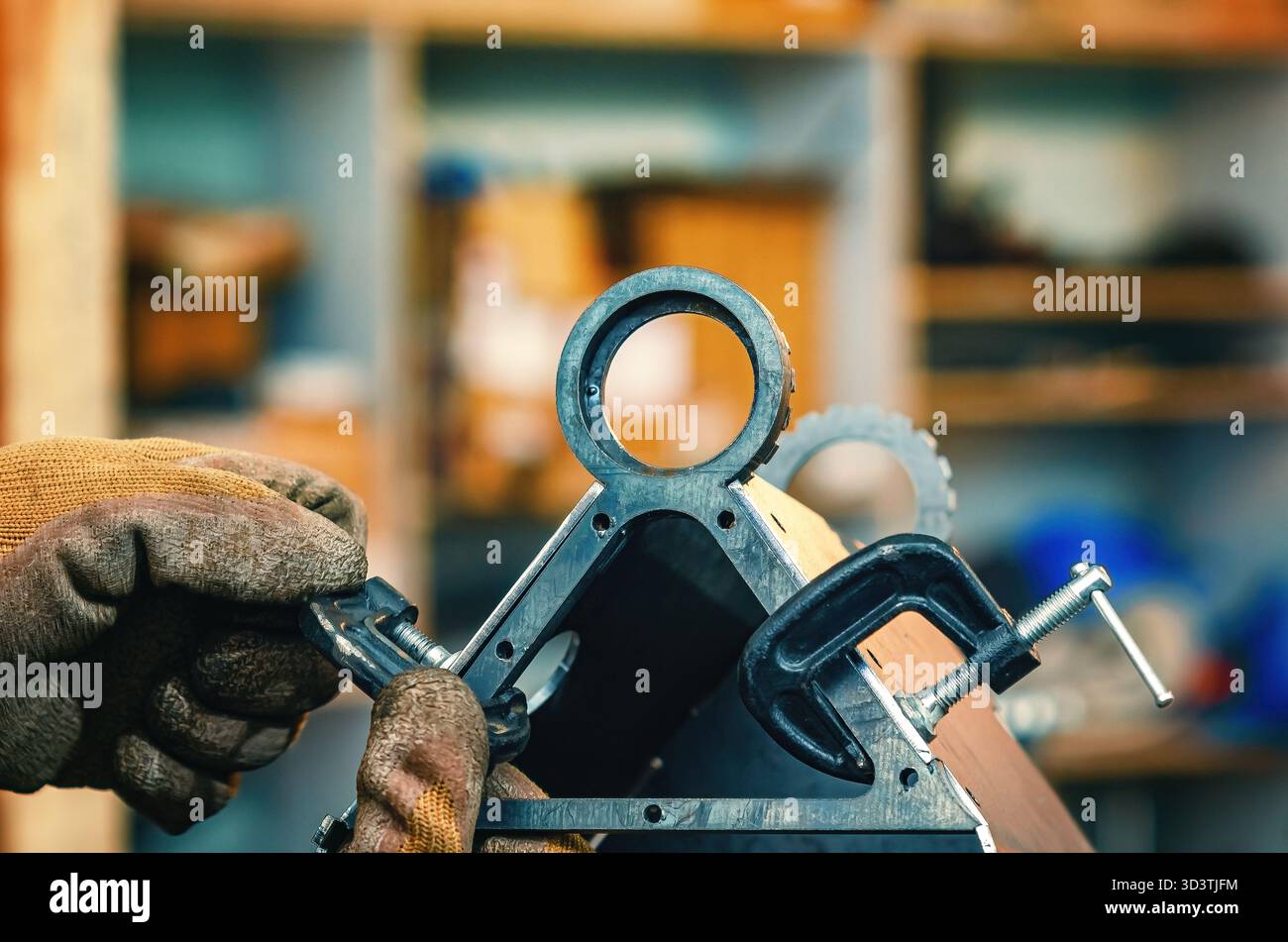 Mit den männlichen Händen werden Metallteile mit einer Schelle festgezogen. Die Schelle verfügt über eine Gewindeschraube zum Festziehen und Einstellen des Drucks. Hintergrund der Industriewerkstatt. Stockfoto